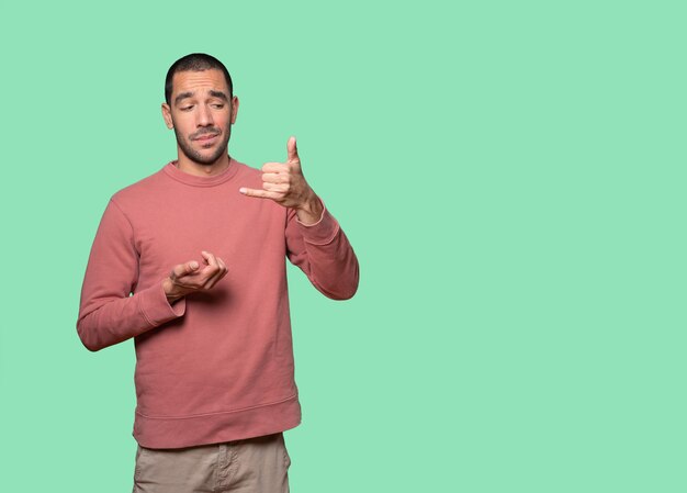 Hesitant young man making a gesture of calling with the hand