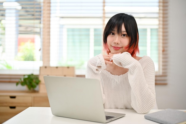 Het aantrekkelijke Aziatische wijfje zit bij haar huiswerkruimte met laptopcomputer
