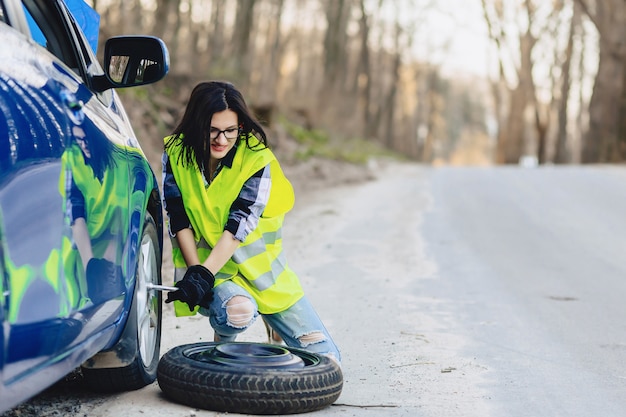 Het aantrekkelijke meisje verwijdert wiel van auto alleen bij weg