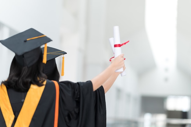 Het achterbeeld van een vrouwelijke studentafgestudeerden die een zwarte hoeden gele leeswijzer dragen