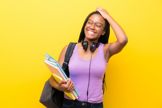 Het Afrikaanse Amerikaanse meisje van de tienerstudent met lang gevlecht haar over het geïsoleerde gele muur lachen