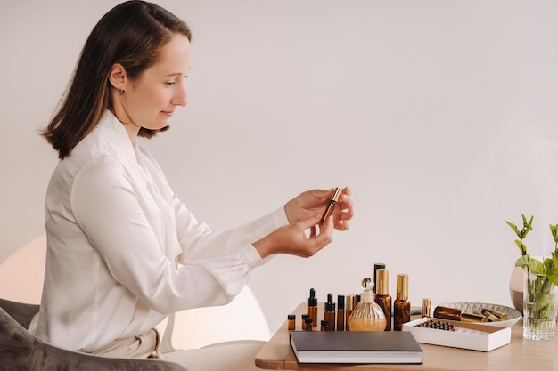 Het aromatherapeut-meisje zit in haar kantoor en houdt een fles aromatische oliën vast, er zijn essentiële oliën op tafel