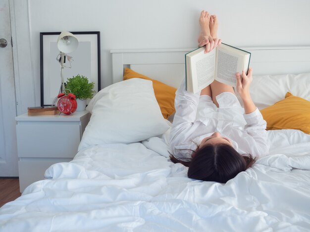 Het Aziatische boek van de vrouwenlezing op bed in de ochtend