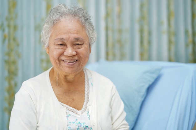 Het Aziatische hogere heldere gezicht van de vrouwen geduldige glimlach terwijl het zitten op bed in het ziekenhuis.