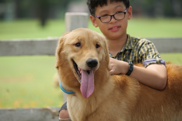 Het Aziatische jongen spelen met gouden retreiver van de puppyhond in park