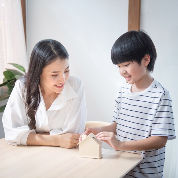 Het Aziatische muntstuk van de zoonshand op moederpalm met besparingscontainer, het mamma van de gelukfamilie en het kind investeren thuis voor onderwijsfinanciën in woonkamer.