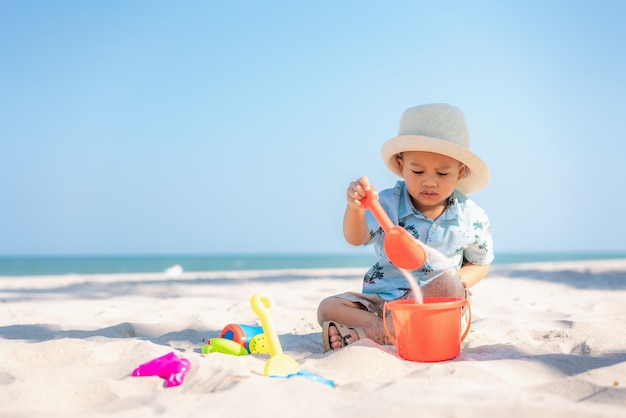 Het aziatische twee éénjarigenpeuterjongen spelen met strandspeelgoed op strand.