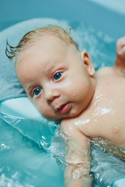 Het baden van een tweemaandige baby in een badkuip het kind ligt op een plastic stand Baby zorg