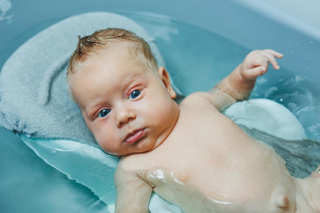 Het baden van een tweemaandige baby in een badkuip het kind ligt op een plastic stand Baby zorg