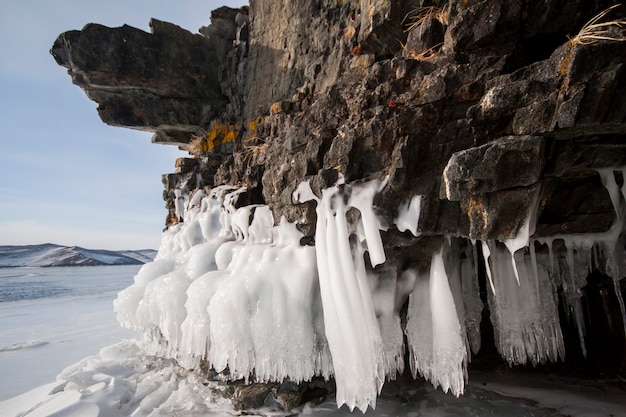 Het Baikalmeer is een ijzige winterdag. Grootste zoetwatermeer. Het Baikalmeer is bedekt met ijs en sneeuw, sterke kou en vorst, dik helderblauw ijs. Aan de rotsen hangen ijspegels. Geweldige plek erfgoed