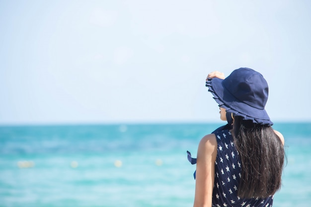 Het beeld achter aziatische vrouwen draagt een hoed op het strand de achtergrond zee.