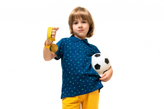 Het beeld van een tiener kaukasische jongen houdt een voetbalbal in één hand en een gouden medaille in andere hand die op witte achtergrond wordt geïsoleerd