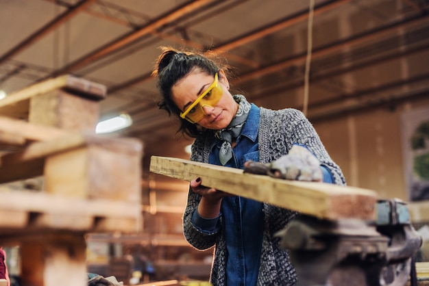 Het beeld van middelbare leeftijd concentreerde vrouwelijke timmerman die en hout kijken voor haar werk in een workshop kiezen.