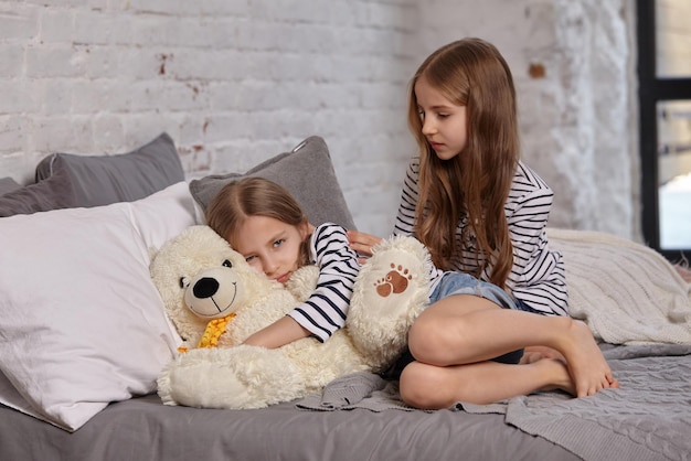 Het beeld van twee kleine zusjes die op het bed in de kamer zitten