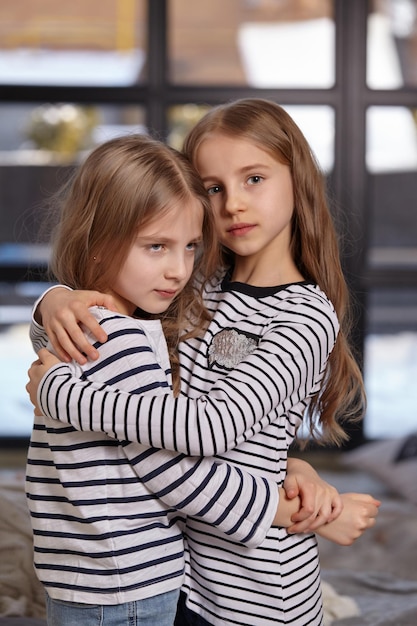 Het beeld van twee kleine zusjes die op het bed in de kamer zitten