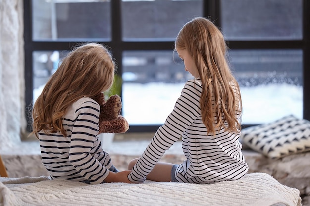 Het beeld van twee kleine zusjes die op het bed in de kamer zitten