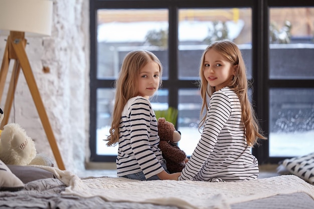 Het beeld van twee kleine zusjes die op het bed in de kamer zitten