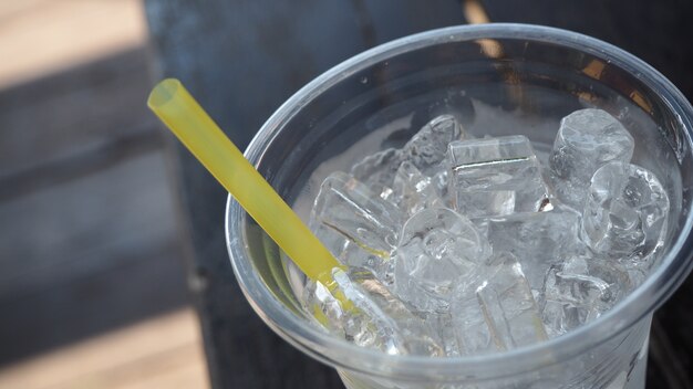 Het beeld van zuiver water met ijs in plastic glas legt op oude houten lijst.