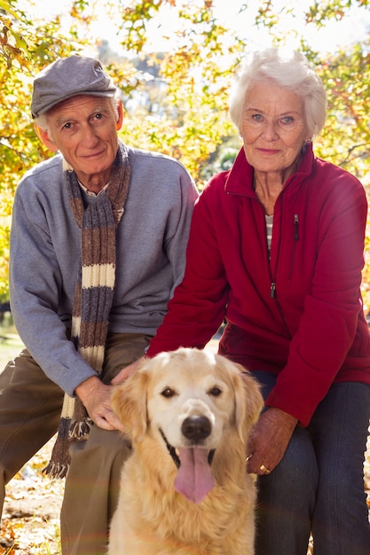 Het bejaarde paar zit en glimlacht bij camera met hond