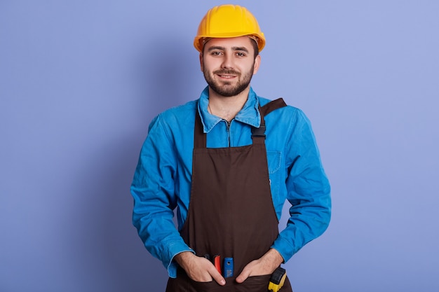 Het binnenbeeld van het knappe vrolijke voorman houden dient zakken in, die uniform dragen, dol op zijn baan, direct camera bekijken, hebbend al materiaal, klaar te herstellen. Ambachtsman concept.