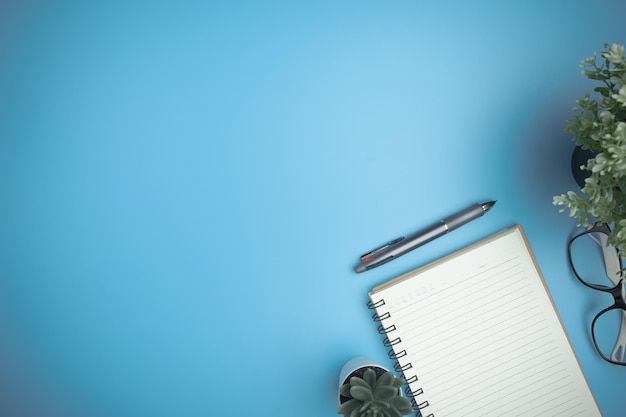 Foto het blauwe bureau met een notitieboekje, een penbril en een miniboom op de blauwe bureau plat lag achtergrond bovenaanzicht werkruimte van tafelkantoor met kopieerruimte bedrijfsstudie leerconcept