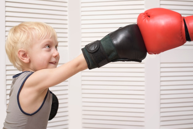 Het blonde jongen in dozen doen met dient rode handschoen in. emoties