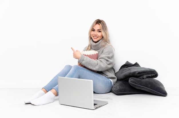 Het blonde meisje dat van de tiener popcorn eet terwijl het letten van een film op laptop die terug wijst