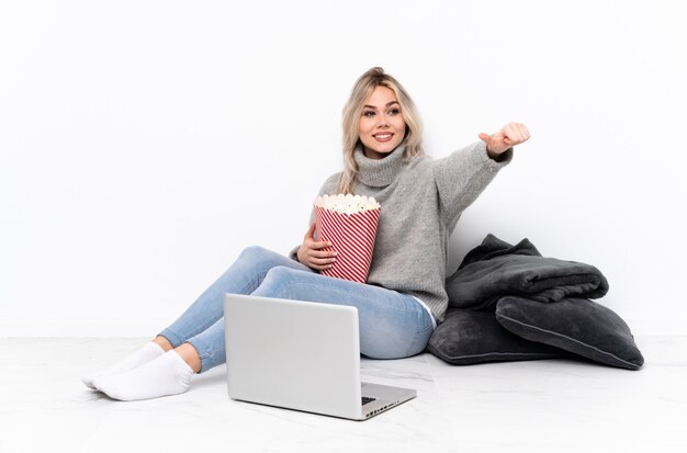 Het blonde meisje dat van de tiener popcorn eet terwijl het letten van een film op laptop geven duimen omhoog gebaar