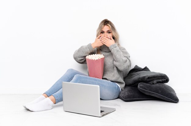 Het blonde meisje dat van de tiener popcorn eet terwijl het letten van op een film op laptop die mond behandelen met handen