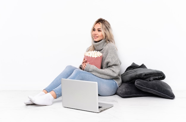 Het blonde meisje dat van de tiener popcorn eet terwijl het letten van op een film op laptop kijkend kant