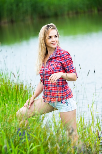 Het blonde meisje heeft plezier in de rivier in rubberen laarzen op het platteland