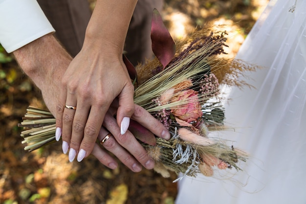 Het boeket van de bruid met gedroogde bloemen in de handen van de pasgetrouwden.