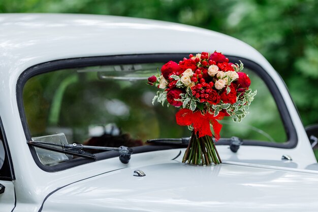 Het boeket van het hartstochtshuwelijk met donkerrode en marsala-rozen, groen dat zich op witte auto bevindt