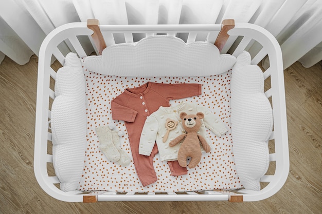 Het bovenaanzicht van babykleding en accessoires in kinderbed, wieg. houten wieg voor pasgeborenen met witte kussens in de babykamer.