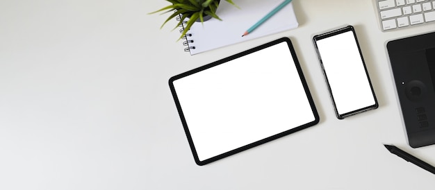 Het bovenaanzichtbeeld van de witte lege tabletcomputer en smartphone zet op een werkruimte.