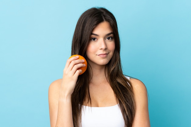 Het Braziliaanse meisje van de tiener over geïsoleerde blauwe achtergrond die een sinaasappel houdt