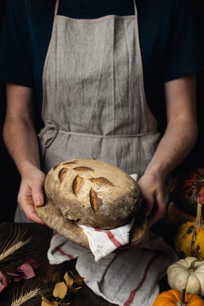 Het broodbrood van de zuurdesem organisch pompoen, vrouwelijke handen op donkere houten lijst