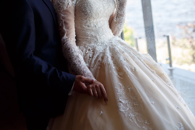 Het bruidspaar houdt zachtjes de handen dicht omhoog. man in pak en vrouw in kanten jurk zachtjes knuffels. hand in hand. trouwdag. romantisch moment