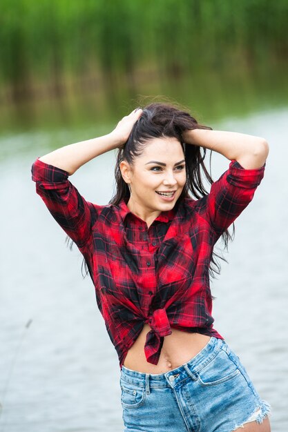 Het brunette meisje heeft plezier in de rivier in rubberen laarzen in het land Jonge vrouw op een meer geniet van het leven