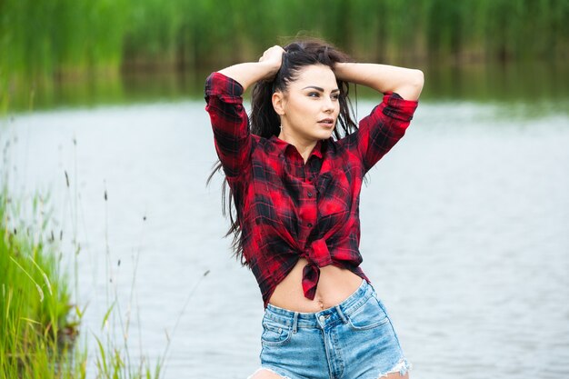 Het brunette meisje heeft plezier in de rivier in rubberen laarzen in het land Jonge vrouw op een meer geniet van het leven