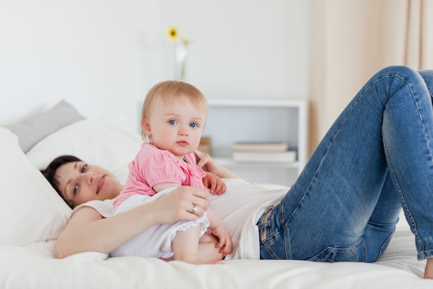 Het charmante donkerbruine vrouw stellen met haar baby terwijl het liggen op een bed