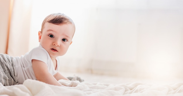 Het charmeren van weinig babyjongen die de camera op witte deken in huis bekijken