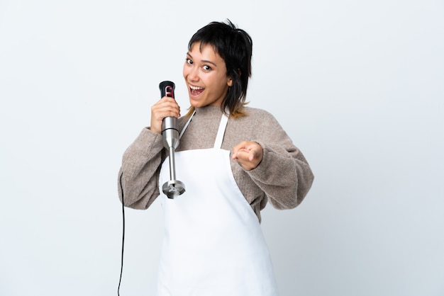 Het chef-kokmeisje die handmixer over geïsoleerde witte punten gebruiken vingert u