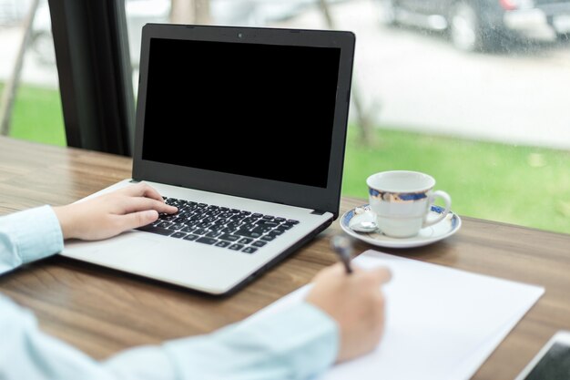 Het close-up van bedrijfswijfje dat met laptop werkt maakt een nota in koffiewinkel zoals backgr