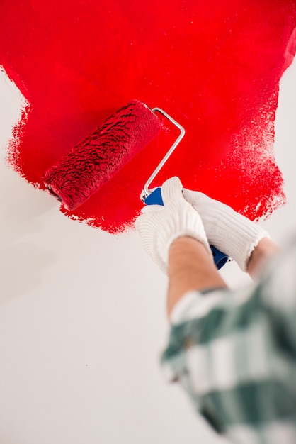 Het close-up van hand met rol schildert een muur in rood.