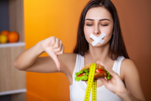 Het concept dieet leuke vrouw met verzegelde mond houdt vettige hamburger