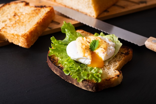 Het concept eigengemaakt Gepocheerd ei van het natuurvoedingontbijt of eieren Benedict op zuurdesembrood dat op zwarte leiraad wordt geroosterd