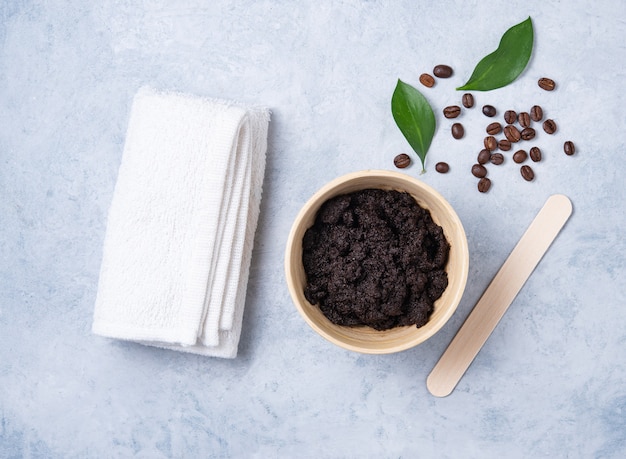 Het concept met natuurlijke ingrediënten voor de koffie van het huislichaam schrobt met koffiebonen en witte handdoek op blauwe achtergrond. Verzorging van de huid van het lichaam. Bovenaanzicht en kopieer ruimte