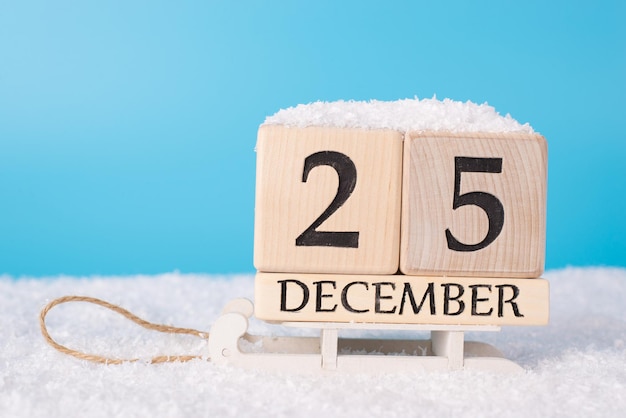 Foto het concept van 25 december is zijn eerste kerstdag. close-up foto van kalender met datum van kerstmis op houten witte sleeën en blauwe lucht