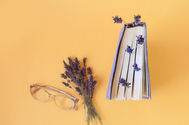 Het concept van aangename herinneringen tijdens het lezen van boeken Gedroogde lavendeltakken tussen de pagina's van een oude boekbril voor visie en een boeket lavendel op een gele achtergrond